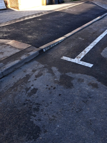 A section of a paved street, showing the dropped kerb, an asphalt patch, and a white line painted on the road. to indicate no parking 